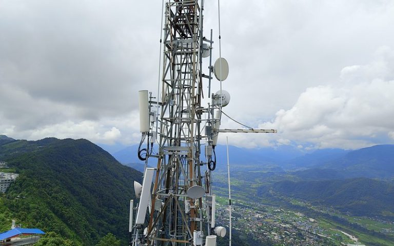Telecommunications tower with antennas and dishes on a hilltop above a valley city