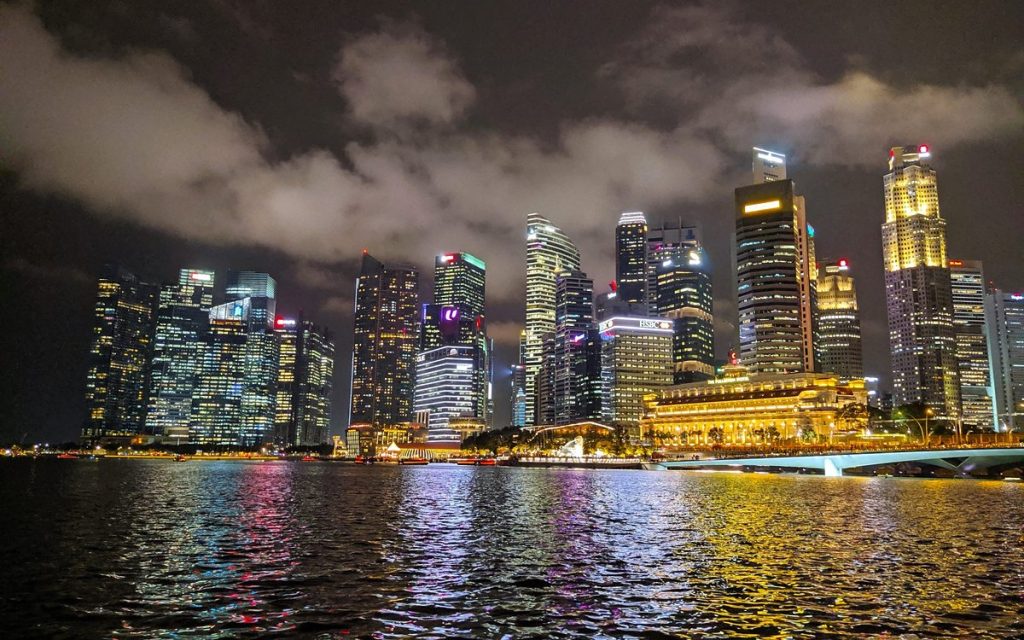 City skyline lit up at night, reflected in the water of a bay