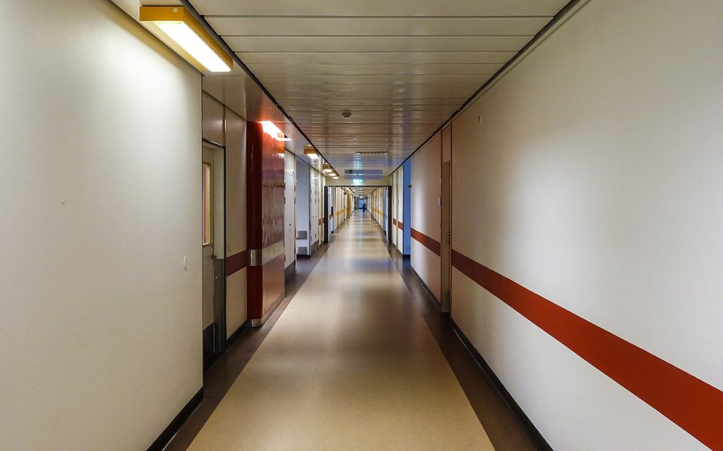 Long, empty hospital corridor with white walls and a red guide stripe