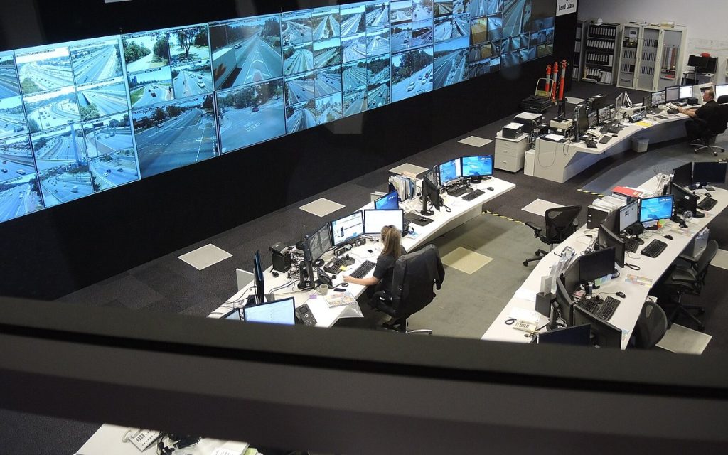 Operators at curved workstations facing a large video wall in a control room