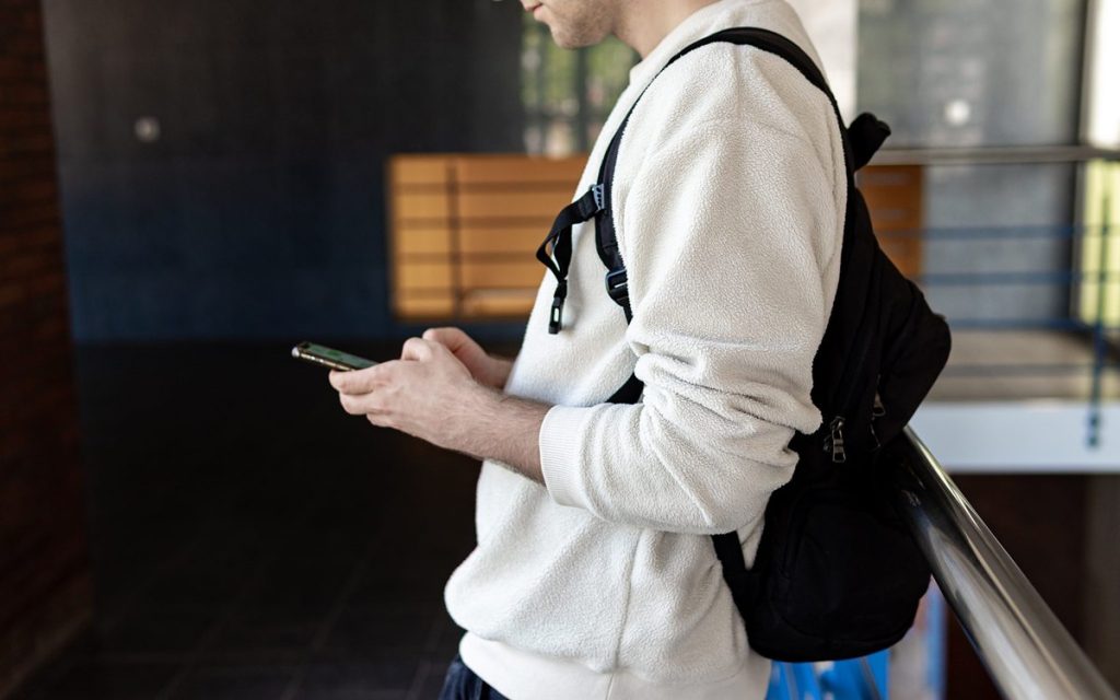 Person with a backpack using a smartphone, face out of frame