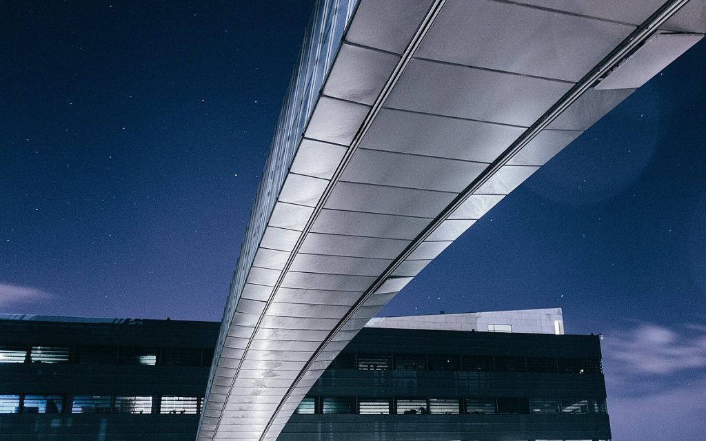 Curved office walkway bridge between modern buildings against a deep blue night sky