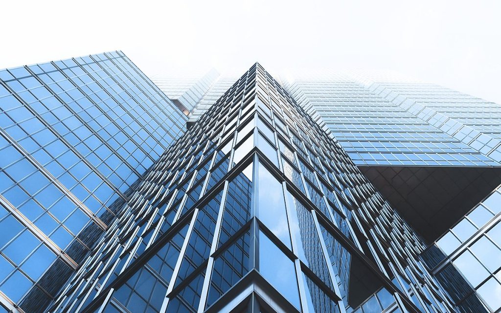 Upward view of a geometric blue glass office tower against a pale sky
