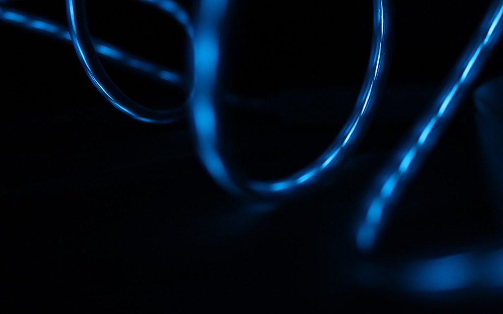 Abstract close-up of glossy wires glowing with blue light against a dark background