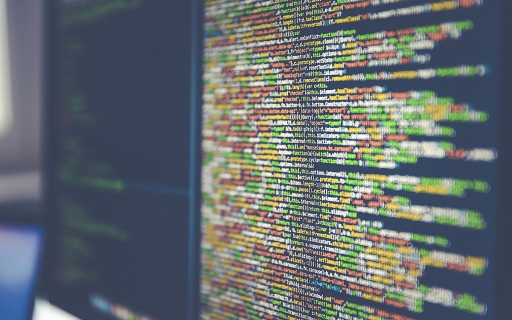 Close-up of a monitor showing lines of colourful source code with shallow depth of field