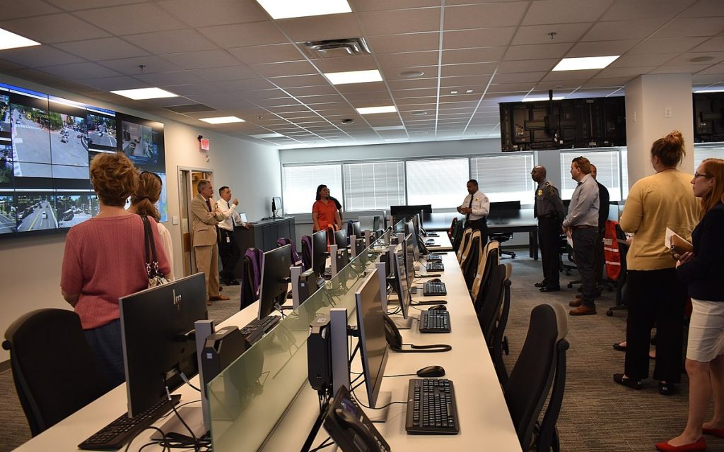 Staff working at rows of computer desks in an operations center with wall-mounted screens