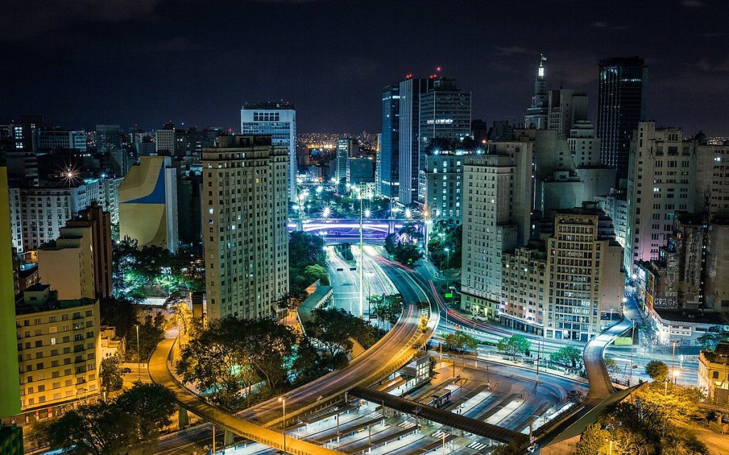 Aerial night view of a dense city with illuminated high-rises and light trails from traffic