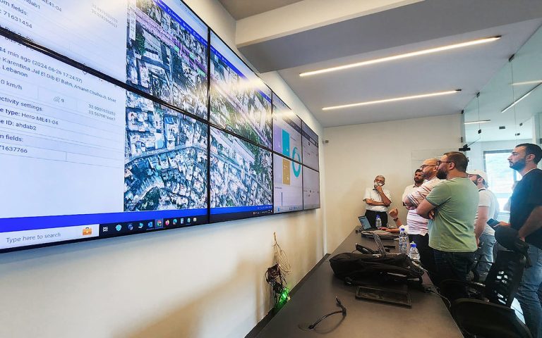 Operations staff gathered in front of a large video wall of maps in a monitoring room