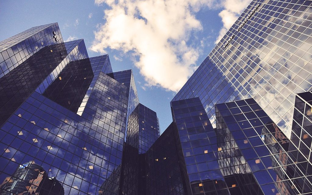 Upward view of reflective blue glass skyscrapers under a partly cloudy sky