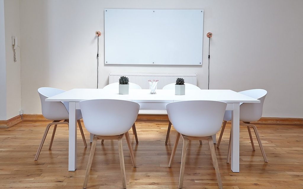 Bright white meeting room with a long table, white chairs and a large wall whiteboard