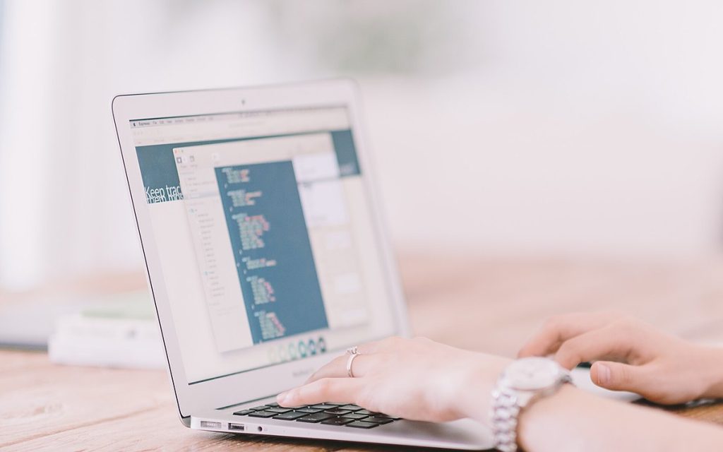 Hands typing on a laptop on a light wooden desk in a bright, softly lit workspace