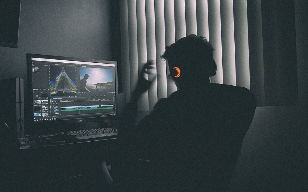 Person seen from behind working at a computer monitor in a dim, dark-walled room